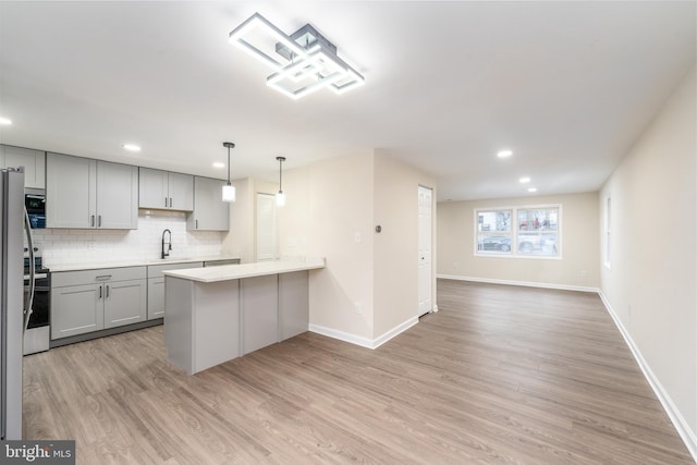 kitchen featuring a peninsula, gray cabinets, light countertops, light wood-type flooring, and backsplash