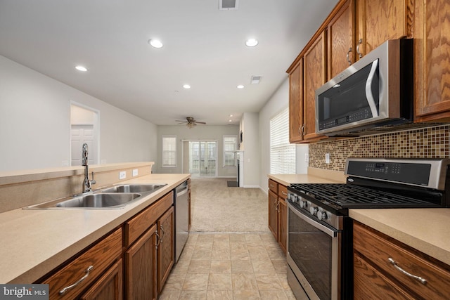 kitchen with brown cabinets, appliances with stainless steel finishes, a sink, and tasteful backsplash