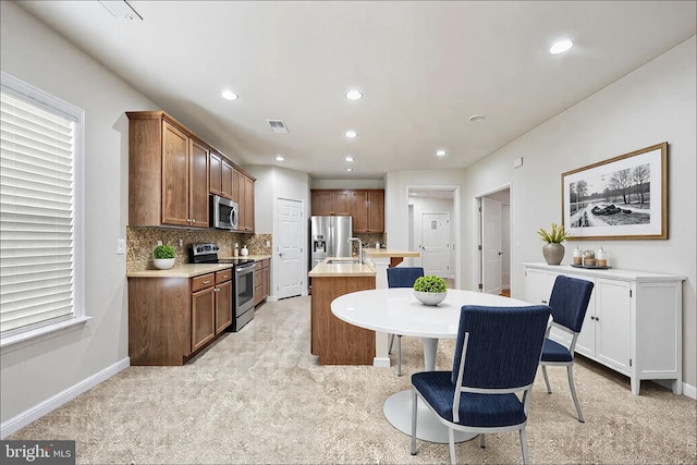 kitchen with stainless steel appliances, visible vents, light countertops, tasteful backsplash, and an island with sink