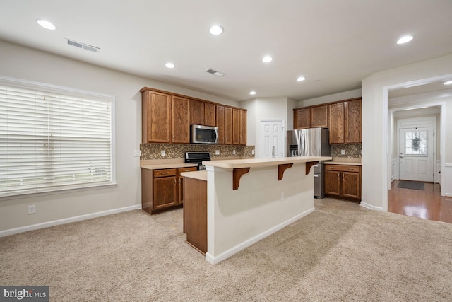 kitchen with appliances with stainless steel finishes, light carpet, visible vents, and a breakfast bar area