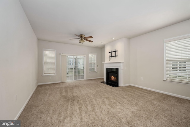 unfurnished living room featuring carpet floors, a fireplace with flush hearth, baseboards, and ceiling fan