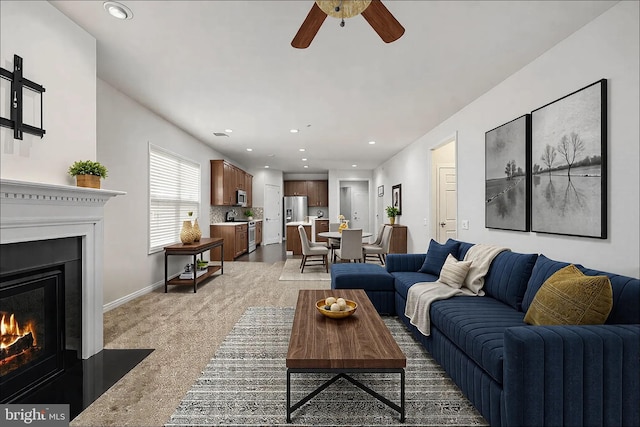 carpeted living room with a ceiling fan, recessed lighting, a warm lit fireplace, and baseboards