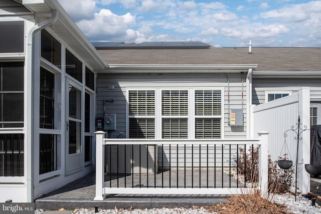 view of side of home featuring fence private yard, a shingled roof, and solar panels