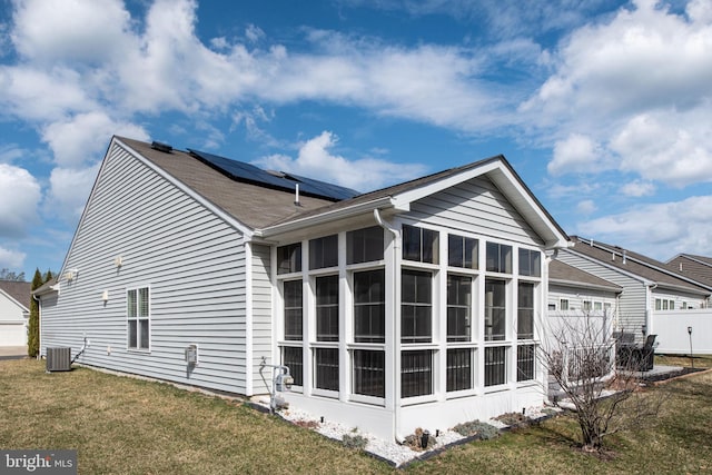 view of side of home featuring central AC unit, an attached garage, solar panels, a sunroom, and a yard