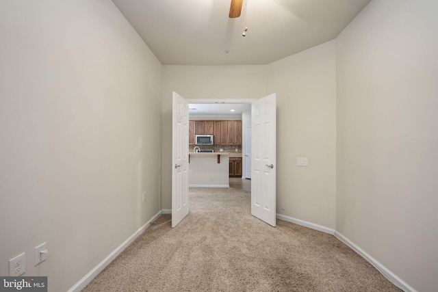 empty room with baseboards, ceiling fan, and light colored carpet