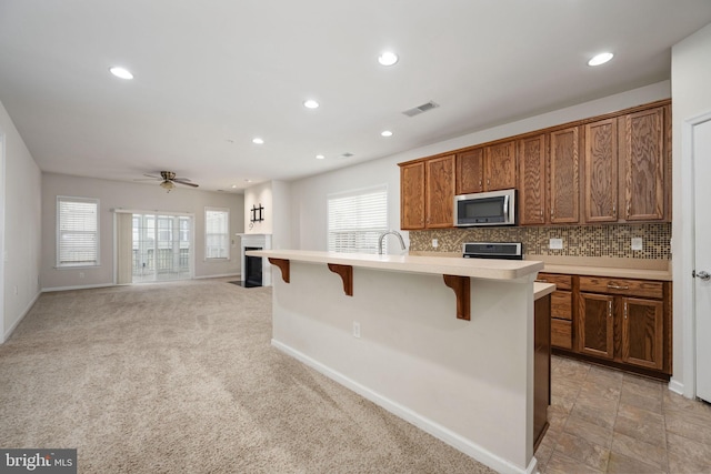 kitchen featuring light countertops, stainless steel microwave, visible vents, decorative backsplash, and a kitchen bar