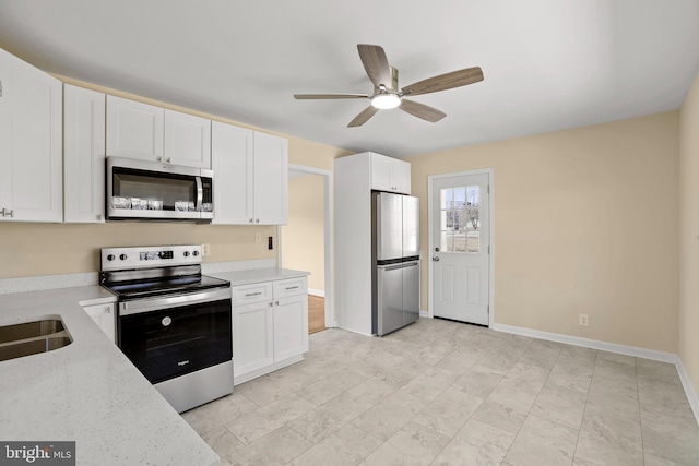 kitchen featuring baseboards, light stone counters, appliances with stainless steel finishes, white cabinetry, and a ceiling fan