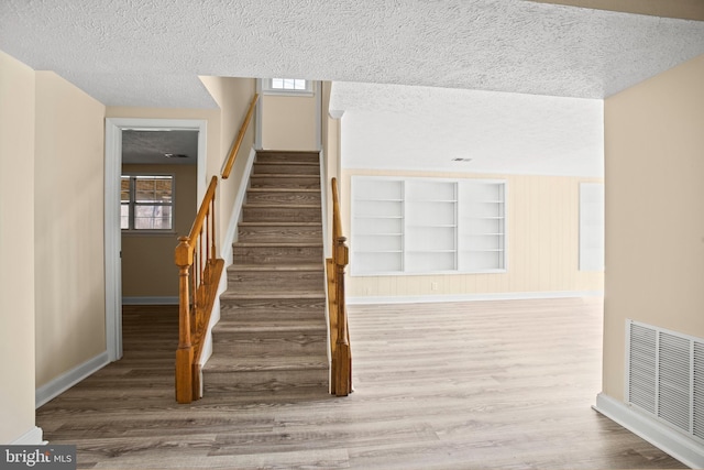 stairs with visible vents, a textured ceiling, baseboards, and wood finished floors