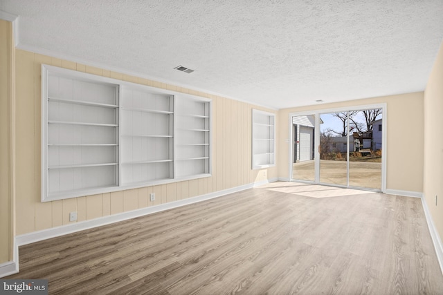 unfurnished living room with visible vents, built in shelves, a textured ceiling, wood finished floors, and baseboards