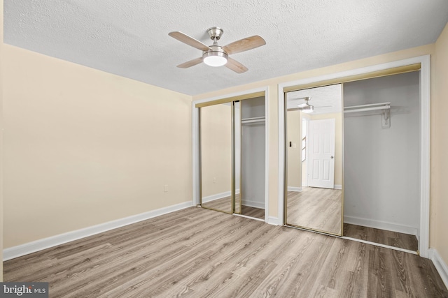 unfurnished bedroom featuring wood finished floors, baseboards, two closets, and a textured ceiling