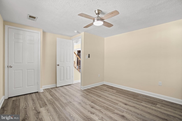 unfurnished bedroom with a textured ceiling, wood finished floors, visible vents, and baseboards