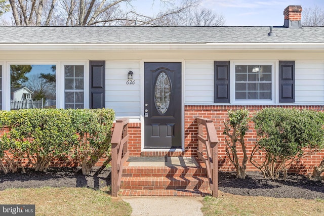 doorway to property featuring brick siding, roof with shingles, and a chimney