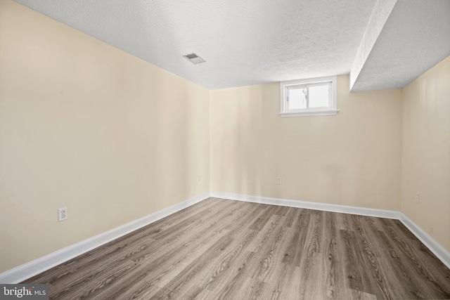 basement featuring a textured ceiling, wood finished floors, visible vents, and baseboards