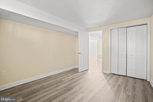 unfurnished bedroom featuring visible vents, baseboards, wood finished floors, a closet, and a textured ceiling