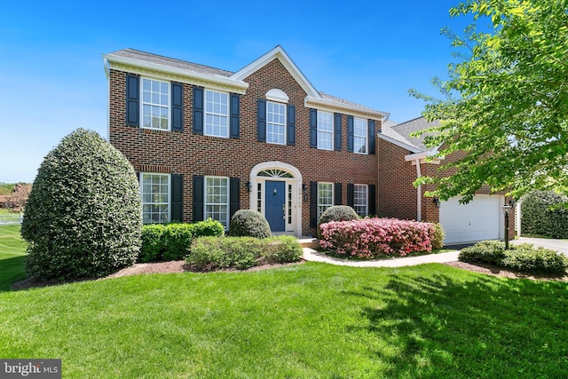 colonial inspired home with a front lawn, an attached garage, and brick siding