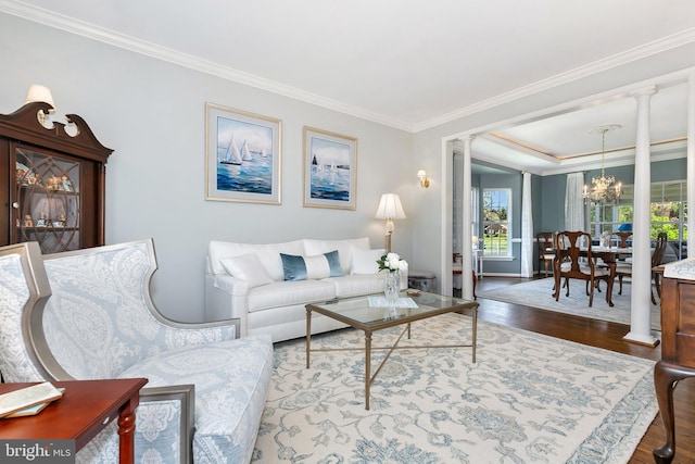living room featuring wood finished floors, an inviting chandelier, decorative columns, baseboards, and crown molding