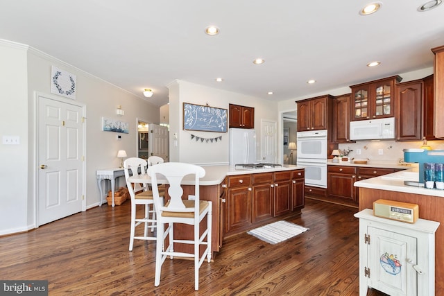 kitchen with white appliances, decorative backsplash, light countertops, a kitchen island, and dark wood-type flooring