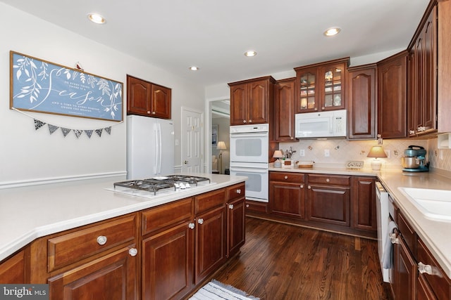 kitchen with dark wood-type flooring, decorative backsplash, white appliances, and light countertops