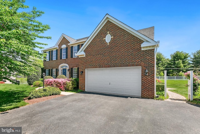 colonial home with fence, a front lawn, driveway, and brick siding