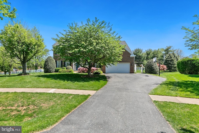 view of property hidden behind natural elements with brick siding, aphalt driveway, and a front lawn