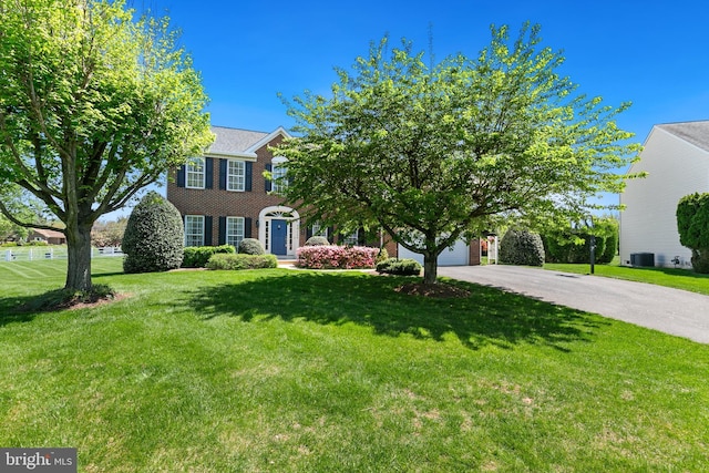 view of front facade with a front yard, concrete driveway, central air condition unit, and brick siding