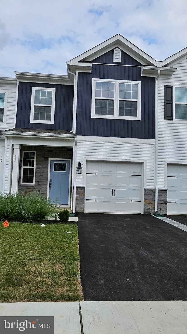 view of property with aphalt driveway, an attached garage, stone siding, board and batten siding, and a front yard