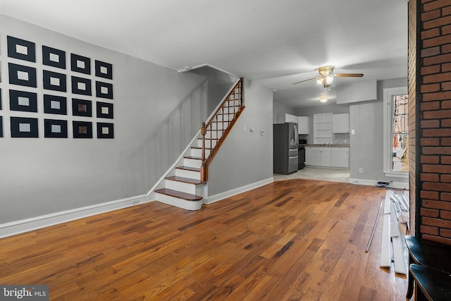 unfurnished living room with wood-type flooring, a sink, ceiling fan, baseboards, and stairs