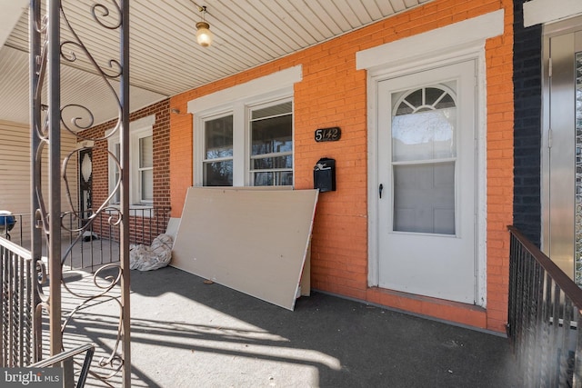 doorway to property featuring a porch and brick siding