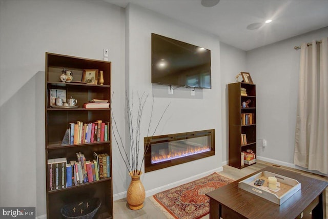 living room featuring a glass covered fireplace, recessed lighting, baseboards, and wood finished floors