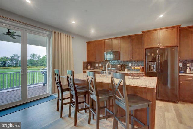 kitchen with range, light wood-style floors, brown cabinetry, and black refrigerator with ice dispenser