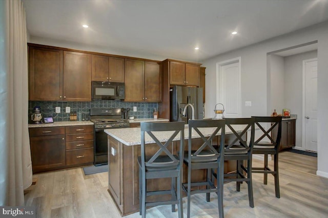 kitchen with black microwave, light wood-type flooring, stainless steel refrigerator with ice dispenser, decorative backsplash, and gas range oven