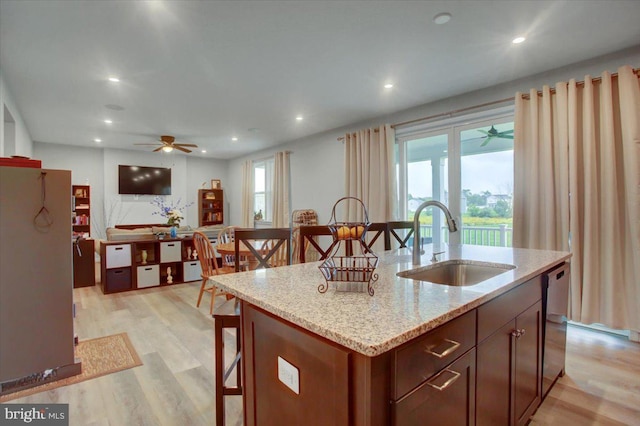 kitchen with light wood finished floors, a breakfast bar area, light stone counters, a sink, and recessed lighting