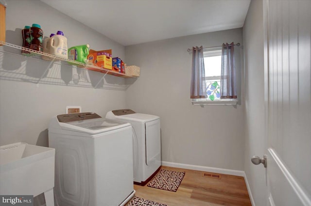 clothes washing area with visible vents, light wood-style floors, a sink, laundry area, and independent washer and dryer