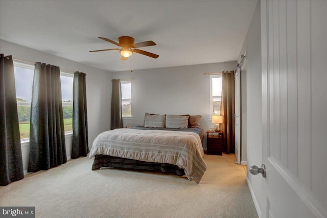 bedroom featuring light carpet, a barn door, multiple windows, and a ceiling fan