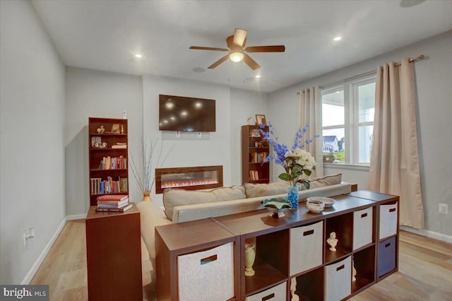 bedroom with light wood-style floors, recessed lighting, baseboards, and a glass covered fireplace