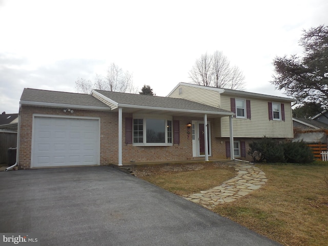 tri-level home with a garage, a front yard, brick siding, and aphalt driveway