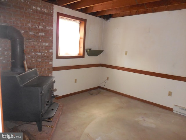 basement with a wood stove, a baseboard radiator, and baseboards