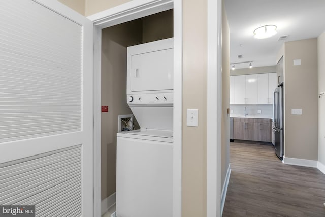 washroom featuring a sink, baseboards, laundry area, stacked washing maching and dryer, and dark wood-style flooring