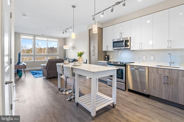 kitchen featuring open floor plan, decorative backsplash, wood finished floors, stainless steel appliances, and a sink