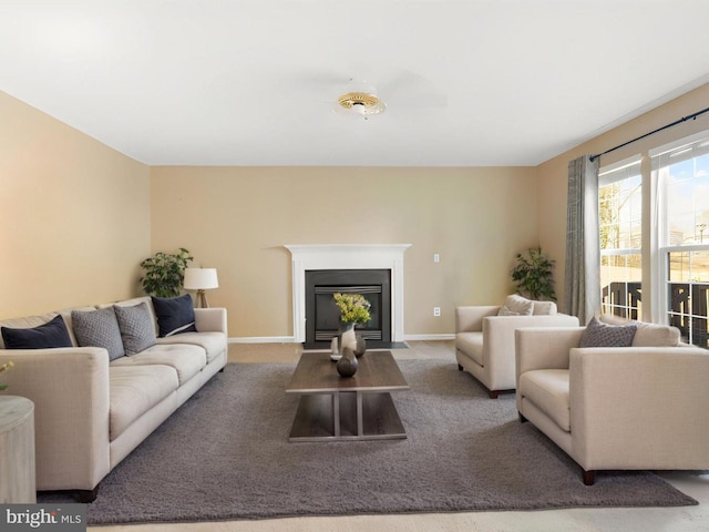 living area with a fireplace with flush hearth, baseboards, and carpet