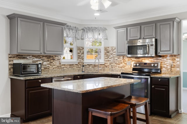 kitchen with gray cabinets, a sink, light stone counters, backsplash, and appliances with stainless steel finishes