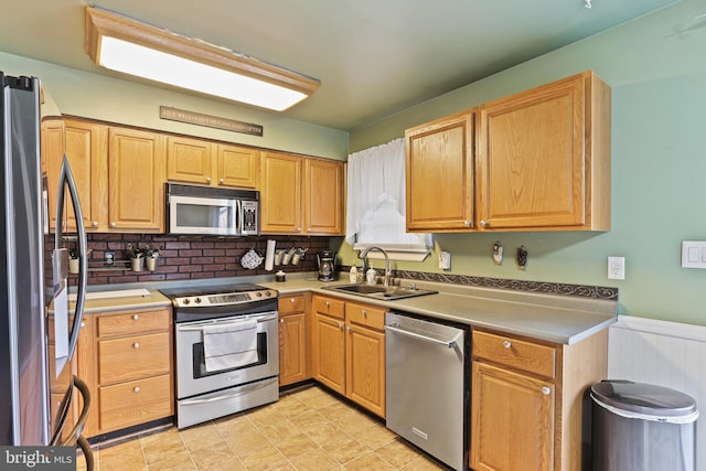 kitchen with a sink, light countertops, appliances with stainless steel finishes, wainscoting, and backsplash