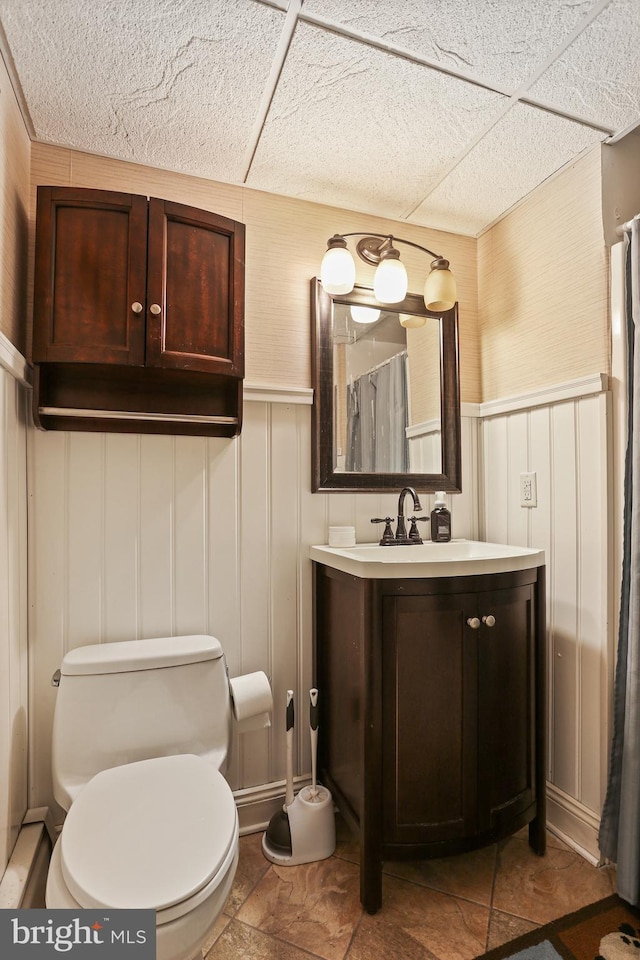 bathroom with a drop ceiling, toilet, a wainscoted wall, a shower with curtain, and vanity