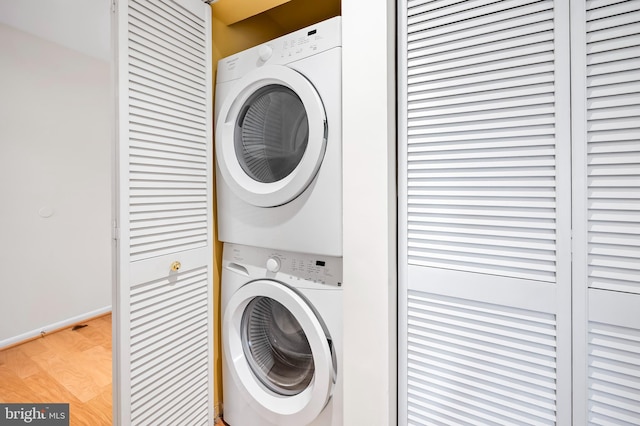 clothes washing area featuring laundry area, light wood-style floors, and stacked washer and clothes dryer