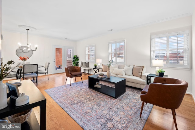 living room featuring a notable chandelier, visible vents, light wood-style flooring, ornamental molding, and baseboards