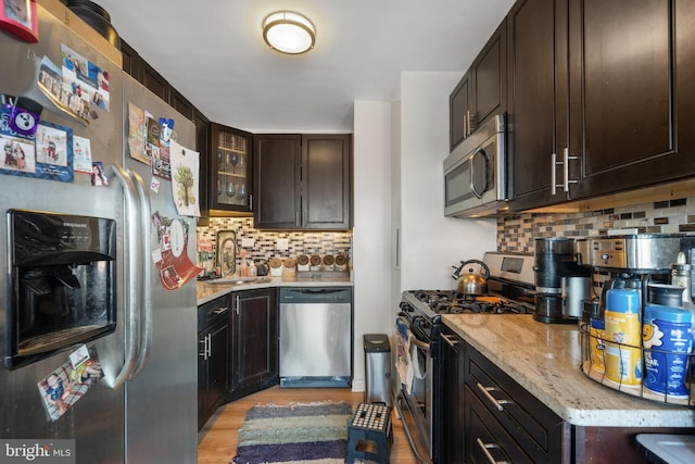 kitchen featuring light wood finished floors, a sink, dark brown cabinetry, appliances with stainless steel finishes, and backsplash