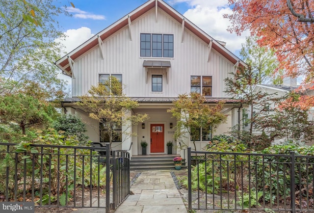 modern farmhouse with metal roof, a fenced front yard, covered porch, a gate, and board and batten siding