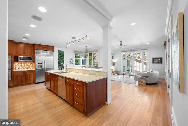 kitchen featuring light wood finished floors, tasteful backsplash, built in appliances, ornate columns, and a sink