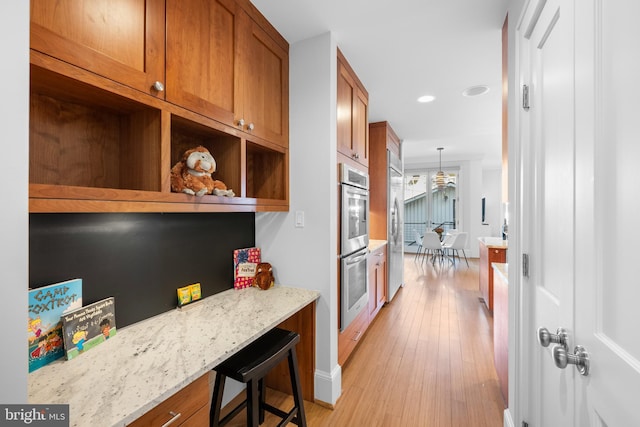 kitchen featuring light wood-style floors, brown cabinets, appliances with stainless steel finishes, and light stone countertops