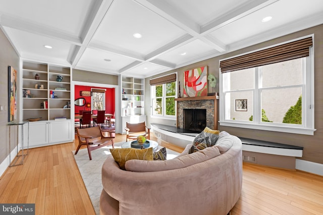 living area featuring light wood-type flooring, coffered ceiling, beamed ceiling, and a fireplace with raised hearth